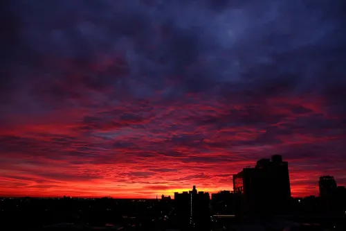 Dramatic sunrise colors display on clouds with city buildings in silhouette in foreground