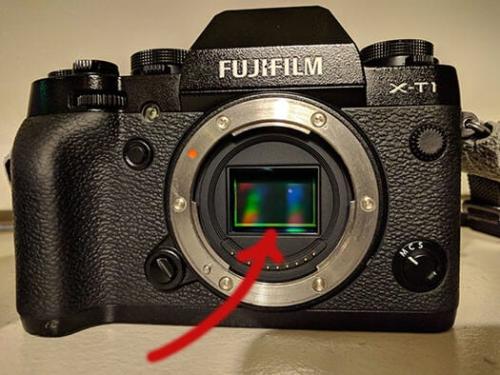 A digital camera with an exposed sensor and an arrow pointing to the sensor